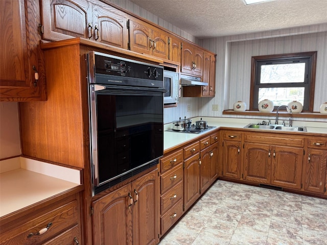 kitchen with brown cabinetry, under cabinet range hood, oven, and a sink
