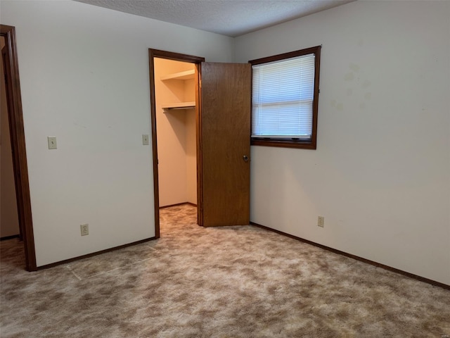 unfurnished bedroom featuring a closet, baseboards, a spacious closet, a textured ceiling, and carpet flooring