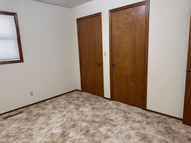 unfurnished bedroom featuring visible vents, baseboards, two closets, a textured ceiling, and carpet floors