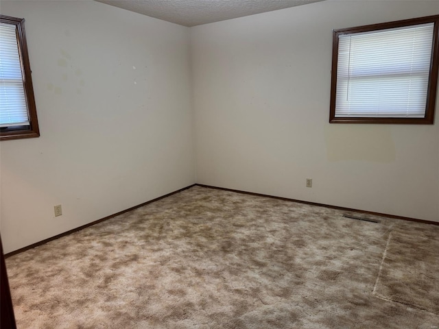 carpeted empty room with visible vents, baseboards, a textured ceiling, and a healthy amount of sunlight