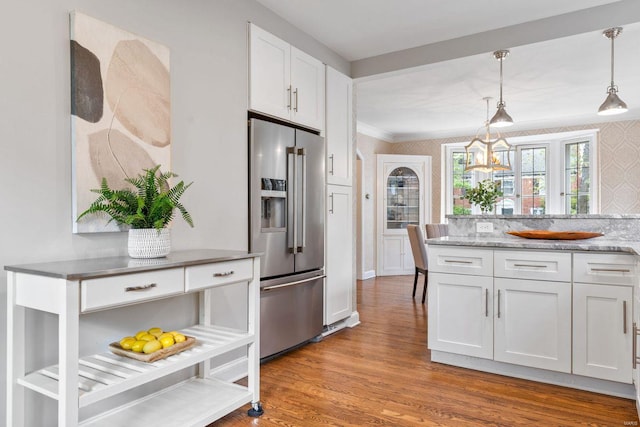 kitchen featuring wood finished floors, high quality fridge, white cabinets, light stone counters, and hanging light fixtures