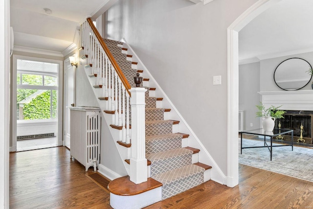 stairway featuring baseboards, ornamental molding, arched walkways, and wood finished floors