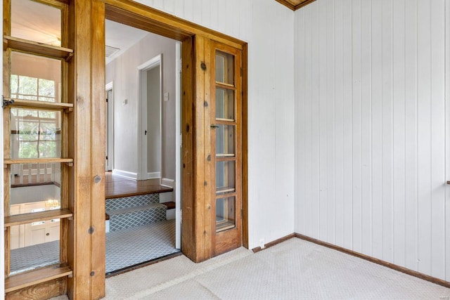 spare room featuring wooden walls, baseboards, and light colored carpet