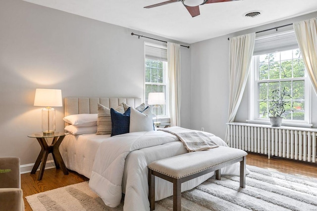 bedroom featuring radiator heating unit, ceiling fan, wood finished floors, and visible vents