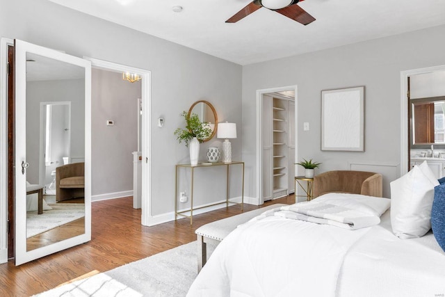 bedroom featuring a sink, wood finished floors, baseboards, a walk in closet, and a ceiling fan