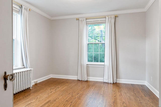spare room with crown molding, baseboards, wood finished floors, and radiator