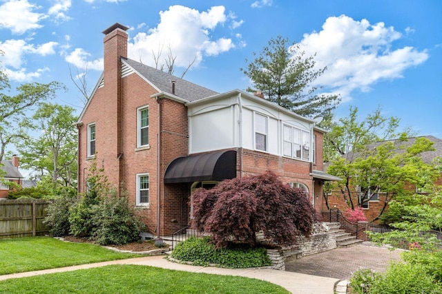 view of front facade featuring brick siding, fence, a chimney, and a front yard