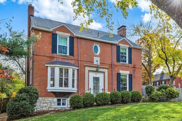view of front of home with brick siding, fence, a chimney, and a front lawn