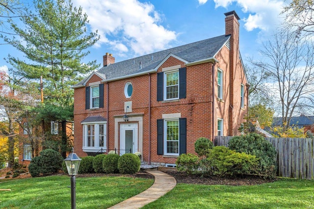 view of front of house featuring brick siding, fence, a front yard, and a chimney