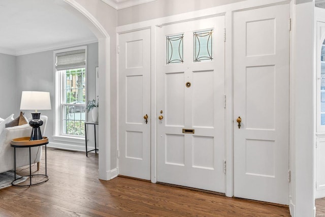 entrance foyer featuring crown molding, arched walkways, wood finished floors, and visible vents