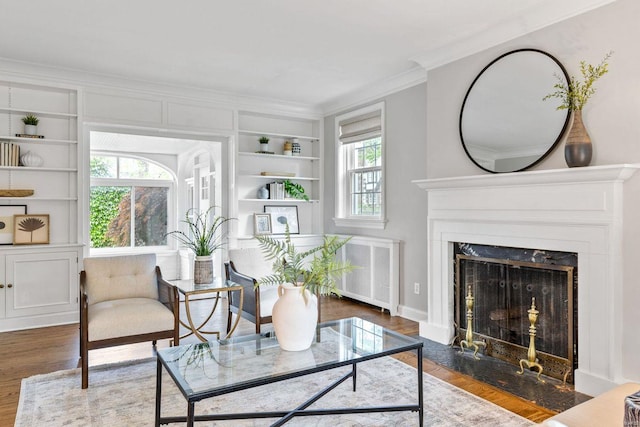 living area featuring crown molding, built in features, wood finished floors, radiator heating unit, and a premium fireplace