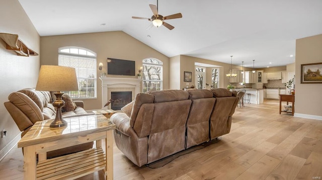 living area with light wood-style floors, a glass covered fireplace, a ceiling fan, baseboards, and lofted ceiling