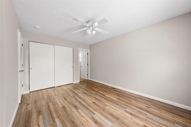 unfurnished bedroom with a closet, baseboards, a textured ceiling, a ceiling fan, and light wood-style flooring
