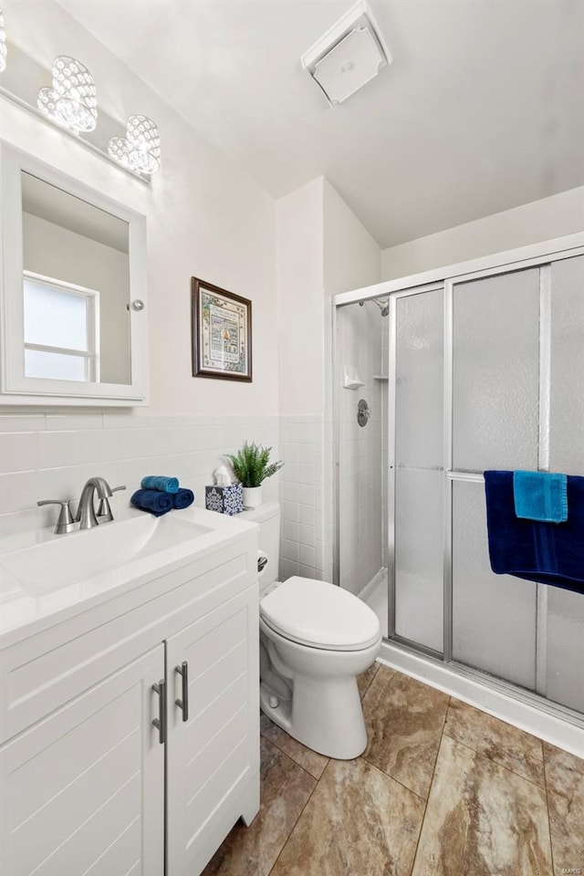 bathroom with wainscoting, vanity, toilet, tile walls, and a stall shower