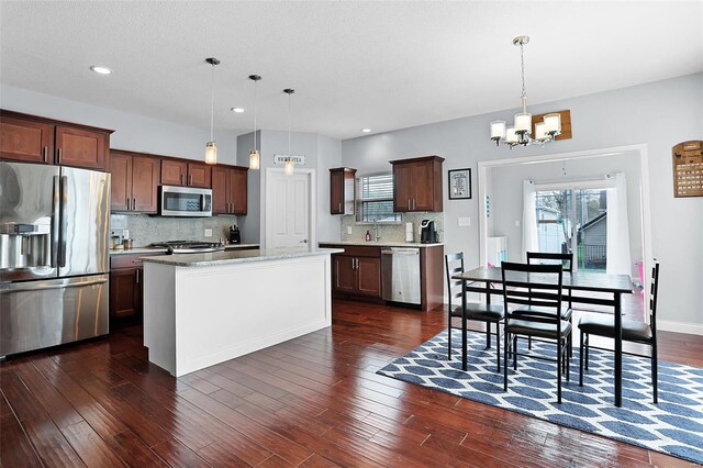 kitchen featuring decorative light fixtures, dark wood finished floors, backsplash, a notable chandelier, and appliances with stainless steel finishes