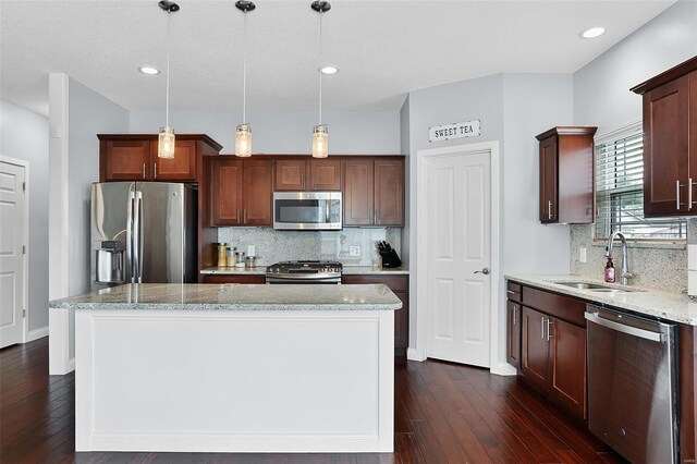 kitchen featuring decorative light fixtures, stainless steel appliances, a center island, dark wood finished floors, and a sink