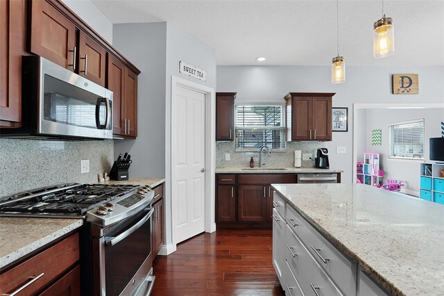 kitchen with decorative backsplash, hanging light fixtures, a sink, dark wood-style floors, and appliances with stainless steel finishes