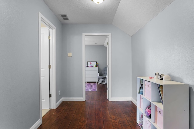 hall with hardwood / wood-style floors, a textured ceiling, baseboards, and visible vents