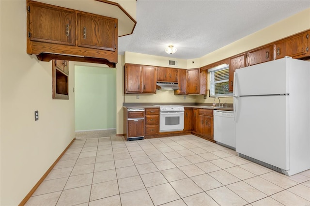 kitchen with white appliances, under cabinet range hood, visible vents, brown cabinetry, and a sink