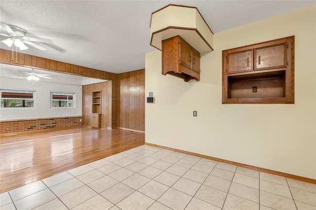 spare room featuring baseboards, a textured ceiling, a ceiling fan, light tile patterned flooring, and wood walls