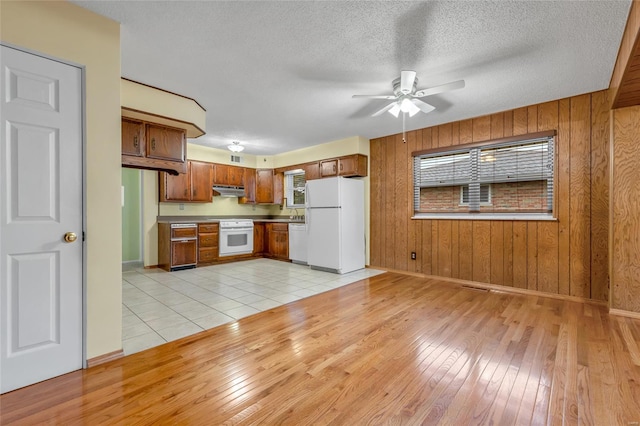 kitchen featuring white appliances, brown cabinets, wooden walls, and a ceiling fan