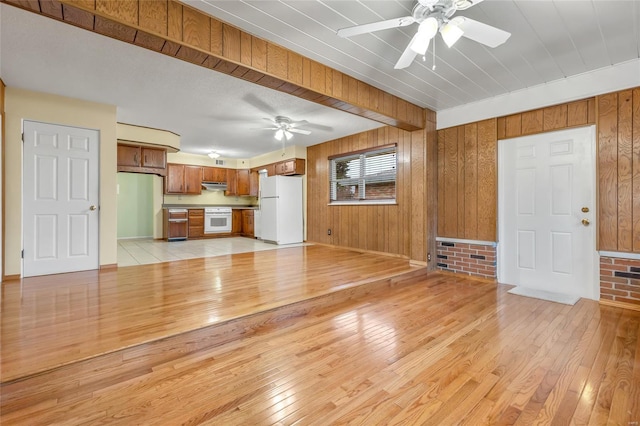 unfurnished living room with light wood finished floors, wood walls, and ceiling fan