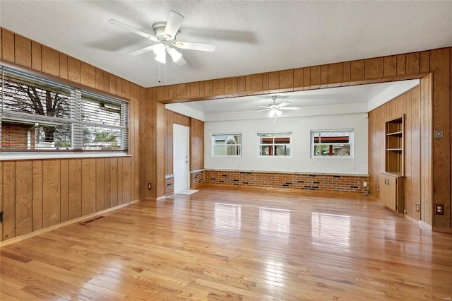 unfurnished living room featuring wood walls, ceiling fan, and visible vents
