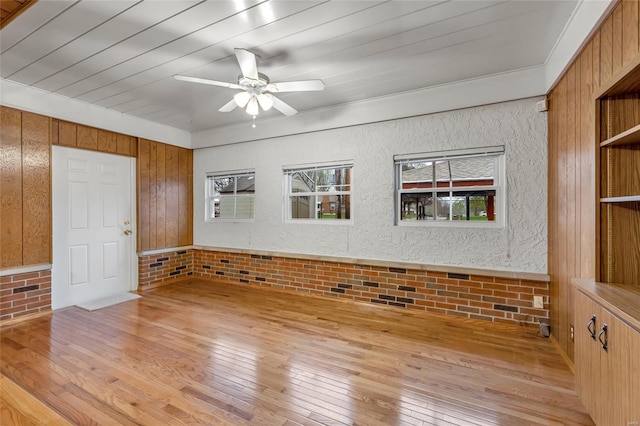 empty room with brick wall, light wood finished floors, a ceiling fan, and wooden walls