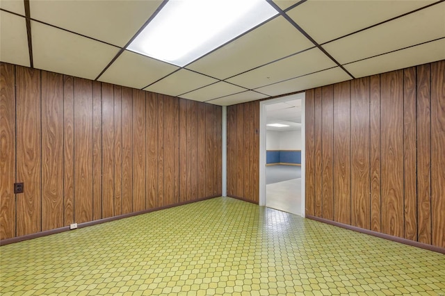 unfurnished room with a paneled ceiling, wooden walls, baseboards, and tile patterned floors