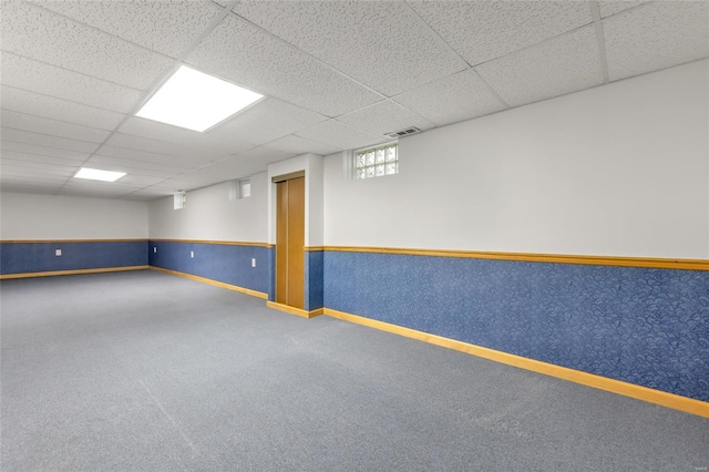 basement featuring carpet floors, visible vents, a drop ceiling, and wainscoting