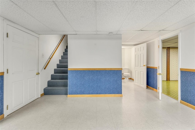 finished basement with stairs, a drop ceiling, baseboards, and light floors