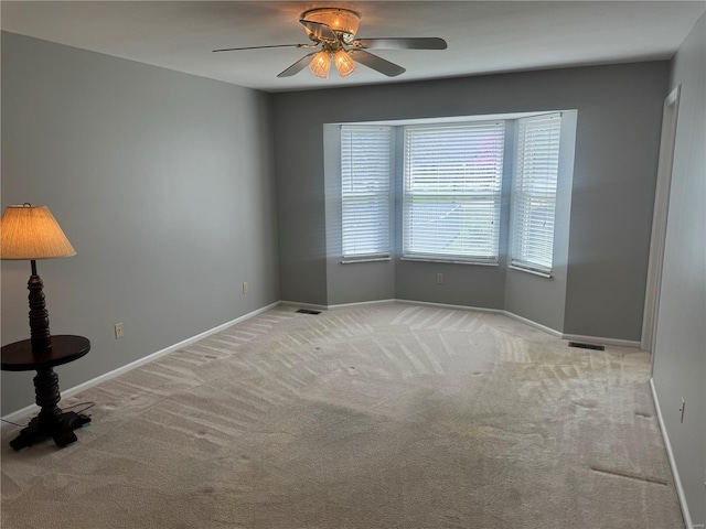 unfurnished room featuring light colored carpet, visible vents, baseboards, and a ceiling fan