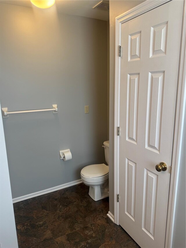 bathroom with baseboards, visible vents, toilet, and stone finish flooring