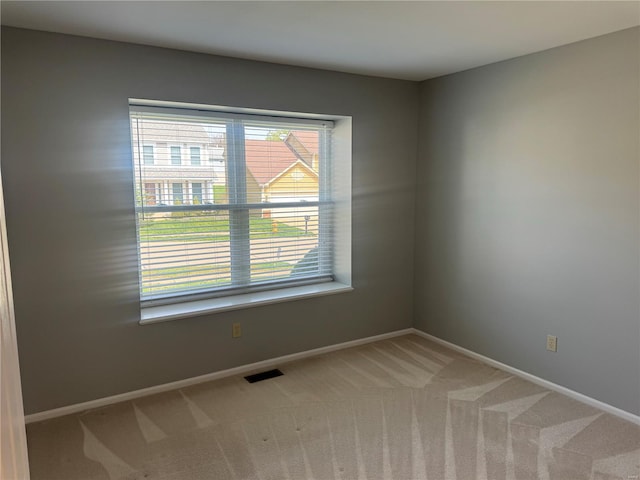 spare room with light colored carpet, visible vents, and baseboards