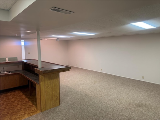 basement featuring dark colored carpet, baseboards, a sink, visible vents, and a paneled ceiling