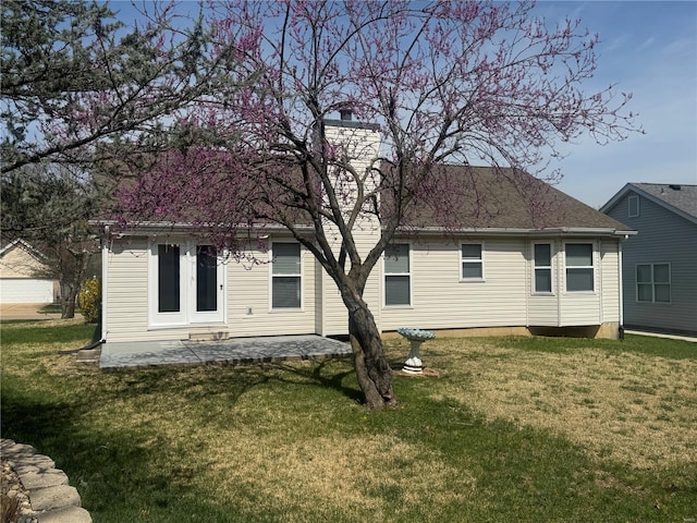 rear view of property featuring a chimney, a patio, a shingled roof, and a lawn