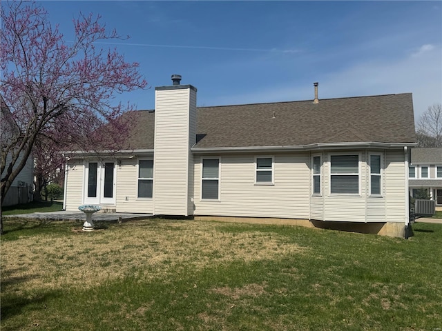back of property with a chimney, a shingled roof, and a yard