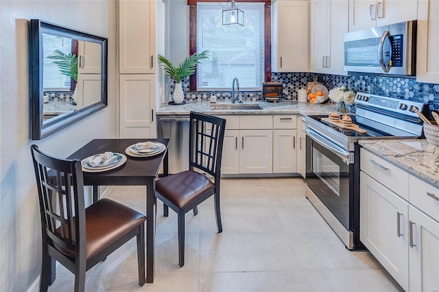 kitchen featuring a sink, white cabinetry, light stone countertops, stainless steel appliances, and decorative backsplash