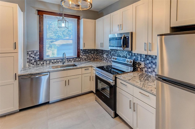 kitchen featuring a sink, backsplash, white cabinets, appliances with stainless steel finishes, and decorative light fixtures