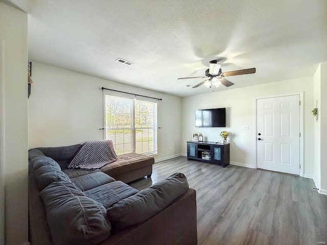 living room with a textured ceiling, a ceiling fan, visible vents, wood finished floors, and baseboards