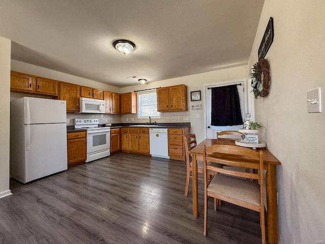 kitchen featuring tasteful backsplash, white appliances, dark countertops, dark wood-type flooring, and a sink