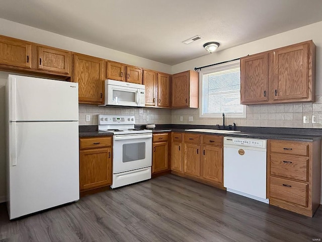 kitchen featuring a sink, white appliances, visible vents, and dark countertops