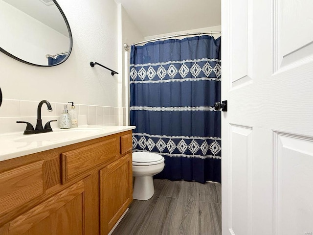 bathroom with a shower with shower curtain, vanity, toilet, tile walls, and wood finished floors
