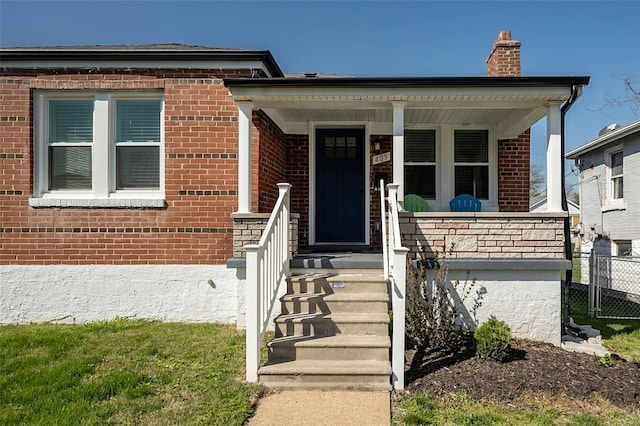 view of front of property with brick siding, fence, covered porch, and a chimney