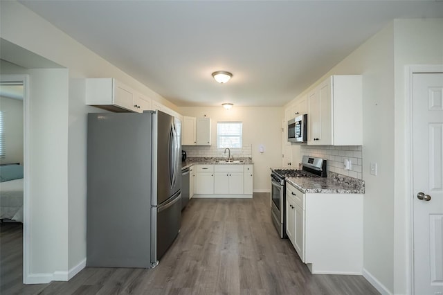 kitchen featuring white cabinets, decorative backsplash, stainless steel appliances, a sink, and wood finished floors