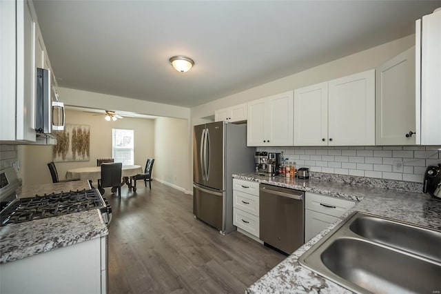 kitchen with white cabinets, a sink, stainless steel appliances, decorative backsplash, and dark wood-style floors