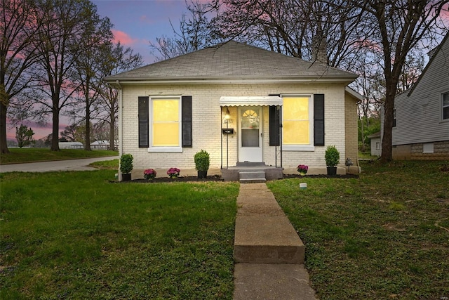 bungalow-style house featuring a yard, a shingled roof, and brick siding