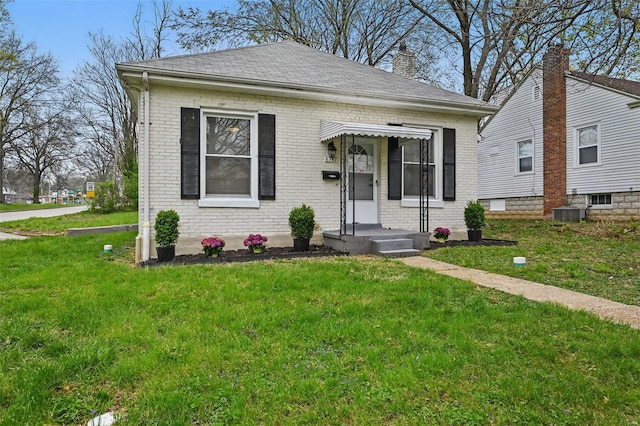 view of front of home featuring roof with shingles, a front yard, brick siding, and a chimney
