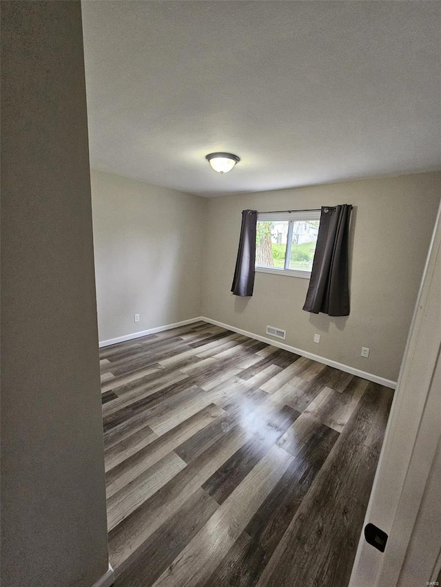 unfurnished room featuring baseboards, wood finished floors, and visible vents