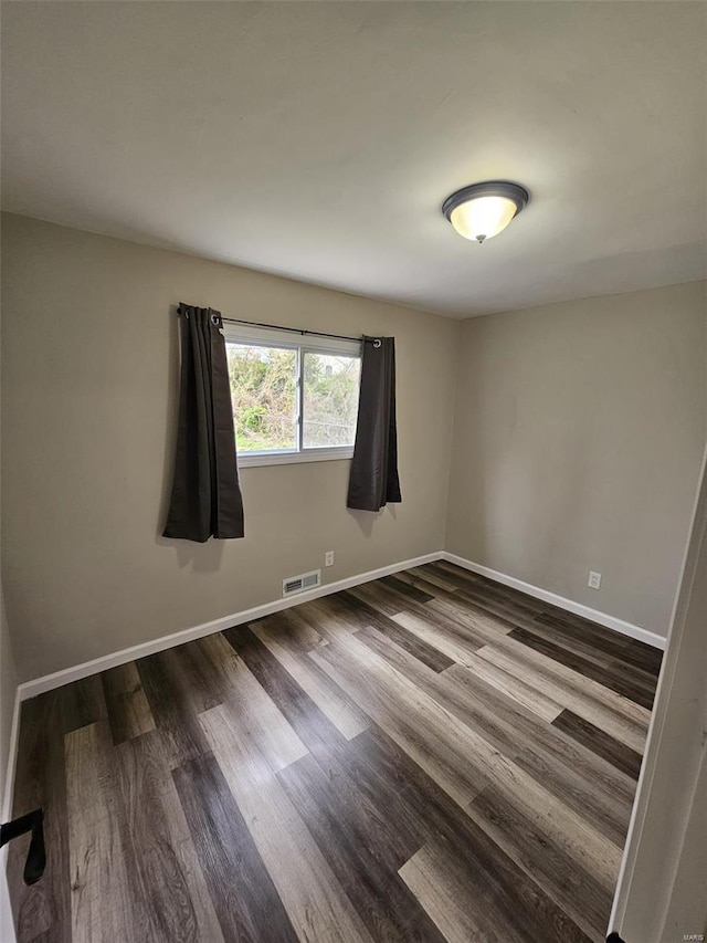 empty room with baseboards, visible vents, and dark wood-style floors